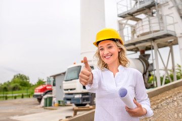 Smiling woman engineer on site, wearing safety helmet, showing thumb up
