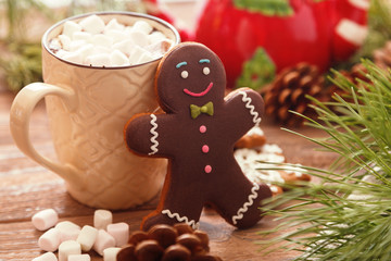 Gingerbread man and hot chocolate with marshmallows, on the background of Christmas tree branches on a wooden table