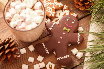 Gingerbread man and hot chocolate with marshmallows, on the background of Christmas tree branches on a wooden table