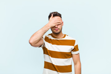 young hispanic man covering eyes with one hand feeling scared or anxious, wondering or blindly...