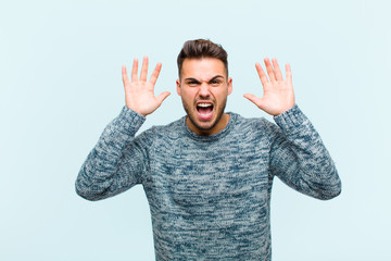 young hispanic man screaming in panic or anger, shocked, terrified or furious, with hands next to...