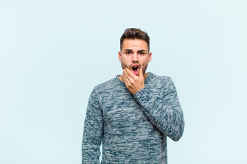 young hispanic man with mouth and eyes wide open and hand on chin, feeling unpleasantly shocked,...