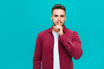 young hispanic man looking serious and cross with finger pressed to lips demanding silence or...