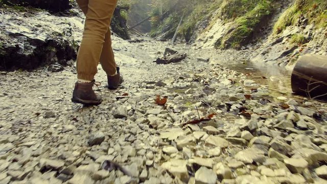 Legs of tourist in trekking boots. Traveler walks along the mouth of  shallow mountain river. Camera follows the traveler's legs. Spirit of adventure. Exploring new places.