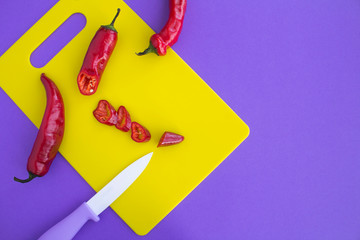 Pepper chile and knife on the yellow cutting board on the violet background. Top view. Copy space.