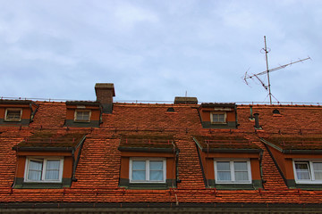 Close-up view of ancient red tile roof with two rows of windows and TV antenna against blue sky. Maribor, Slovenia