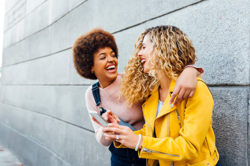 Beautiful lesbian couple using a mobile in the street - Powered by Adobe