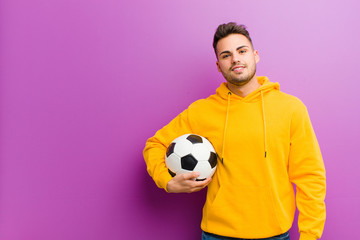 young hispanic man with a soccer ball against purple background