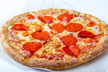 A fresh prepared tasty pepperoni pizza with salami, tomatoes and cheese a on a white background close up. Italian traditional lunch or dinner.