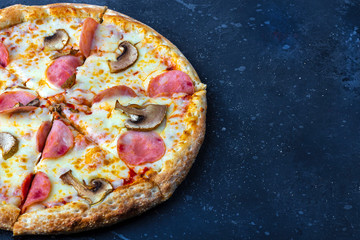 A fresh prepared pizza with with mushrooms, ham and cheese on a dark background. Italian traditional lunch or dinner. Fast food and street food concept. Flat ly, top view, copy space fot text