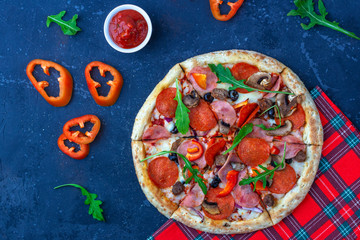 A fresh prepared pizza with salami, mushrooms, ham and cheese on a dark background. Italian traditional lunch or dinner. Fast food and street food concept. Flat ly, top view, copy space fot text