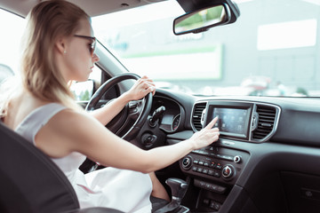 Girl driving car in cabin. Presses on touch screen, selects application. Activate and enable navigation. In summer in city in parking lot near shopping center.