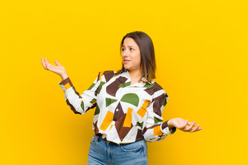latin american woman shrugging with a dumb, crazy, confused, puzzled expression, feeling annoyed...