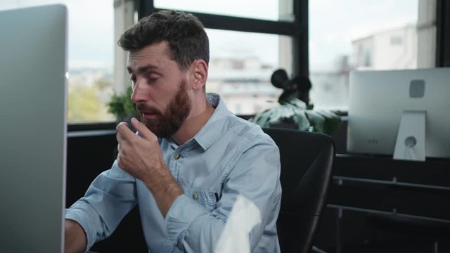 Sick exhausted caucasian business man working by computer sneezing with allergy suffering from illness using napkins.