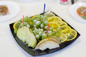 Fruit for the buffet on a white plate. Grapes, lemon, apple for snack