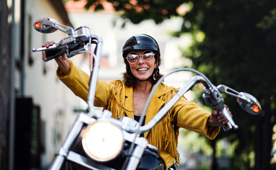 Cheerful senior woman traveller with motorbike in town.