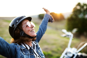 A cheerful senior woman traveller with motorbike in countryside.