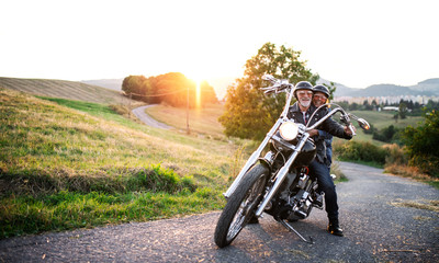 Fototapeta na wymiar A cheerful senior couple travellers with motorbike in countryside.