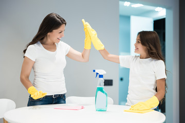 young beautiful woman and her cute teen daughter in yellow gloves doing cleaning wiping dust off...