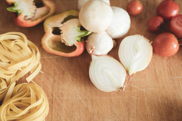 Italian cuisine background, with tomatoes, spaghetti, mushrooms, peppers, onions on a wooden brown board