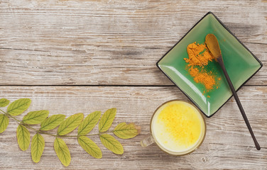 Cup with golden milk and a plate with turmeric and a spoon on a wooden background. Nearby are...
