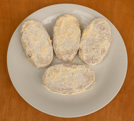 Cutlet on a plate in the cooking process, sprinkled flour on them and ready for frying