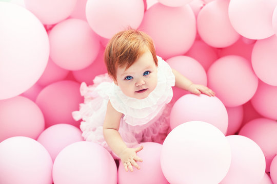 beautiful, 11 month baby girl standing among pastel pink balloons