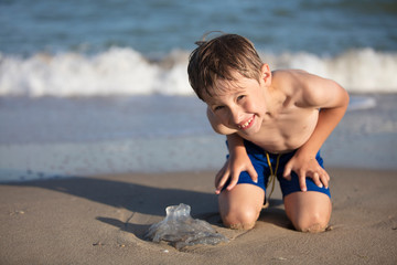 A boy near the sea examines a jellyfish. Child resting on the beach
