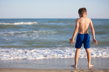 A boy near the sea is considering the waves. Child resting on the beach