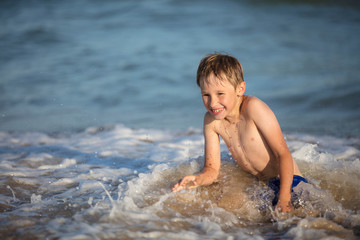 Joyful boy near the sea plays with the waves. Child resting on the beach