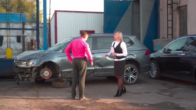 A man in a car service agrees repair with a young woman agent. Inspection of the car after an accident. Conversation with an insurance expert. Compensation for losses after an accident.