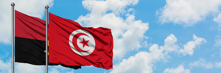 Angola and Tunisia flag waving in the wind against white cloudy blue sky together. Diplomacy...