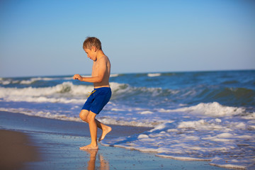 Fototapeta na wymiar A child plays on the beach. A boy runs by the sea. Active holiday on the beach