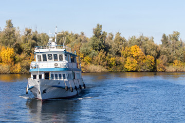 imlittle white steamboat walking along a large autumn river