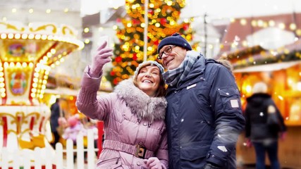 technology, winter holidays and people concept - happy senior couple taking selfie by smartphone at christmas market on town hall square in tallinn, estonia - Powered by Adobe