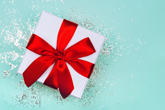 Gift box with red bow on green mint background with delicate golden sparkles.