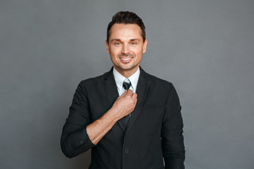 Businessman studio standing isolated on grey fixing tie looking camera happy