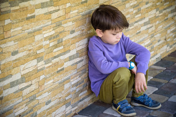 Little boy sad sitting alone at school hides his face. Isolation and bullying concept. Kid sad and unhappy, child was crying, upset, feel sick