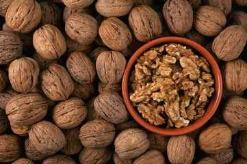 Pile of walnuts and peeled nuts in bowl. View from above.