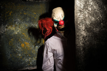 scary clown, in the shadows, looking eerily at the camera from behind an abstract wall. Halloween...