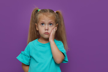 Sad little child girl suffering from toothache isolated on purple background. Upset child with...