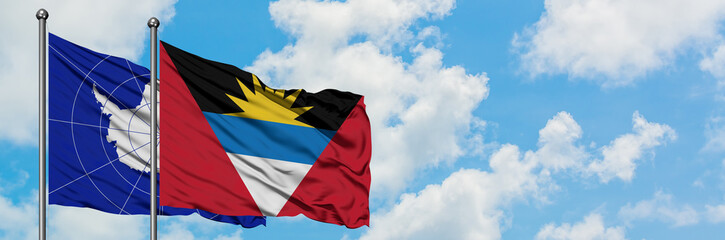 Antarctica and Antigua and Barbuda flag waving in the wind against white cloudy blue sky together. Diplomacy concept, international relations.