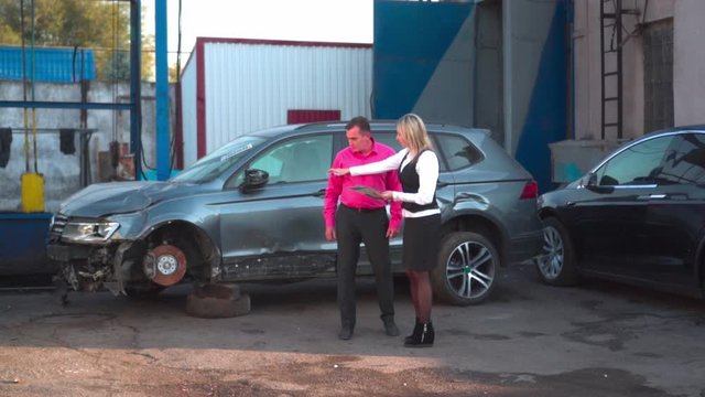 A man in a car service agrees repair with a young woman agent. Inspection of the car after an accident. Conversation with an insurance expert. Compensation for losses after an accident.