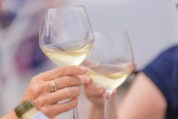 Photo detail of two hands together holding two glasses of white wine. Concept of celebration.