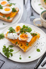 Bruschetta with pumpkin puree, boiled eggs, fresh basil and cream cheese on grey linen textile. Cup of coffee on the background. 