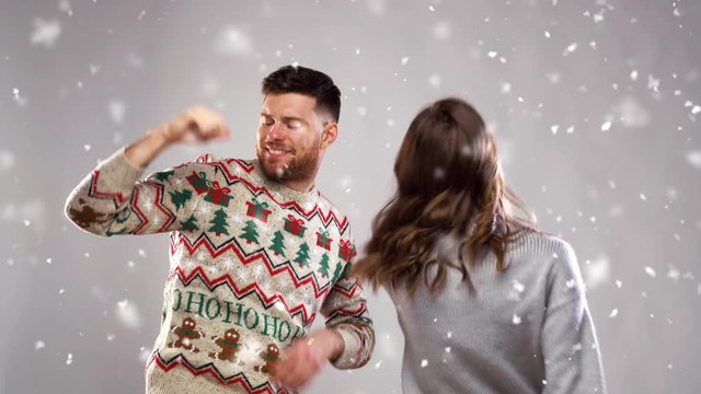 celebration, fun and holidays concept - happy couple wearing knitted sweaters dancing at christmas party