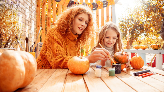 Happy woman drawing on pumpkin with her little daughter
