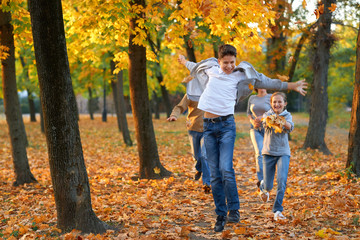 Fototapeta premium Happy family having holiday in autumn city park. Children and parents running, smiling, playing and having fun. Bright yellow trees and leaves