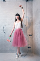 Young woman in white tank top, pink chiffon skirt and white sneakers striking a ballerina pose...