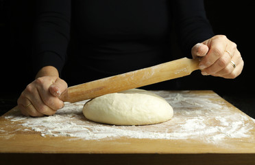 Preparare la tradizionale pasta fatta in casa. Primo piano delle mani della donna con il matterello e la pasta fresca sulla tavola infarinata.